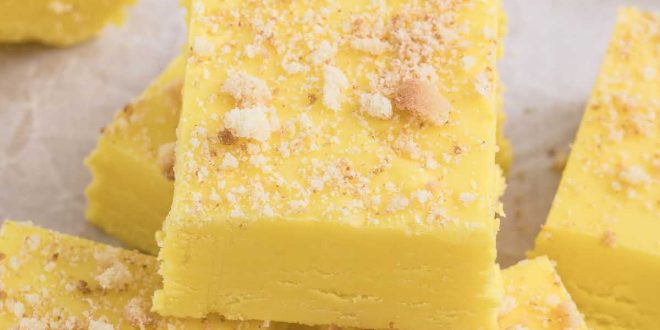 Leuchtend gelbes, cremiges Bananen-Fudge in Quadrate geschnitten und mit Keksbröseln garniert auf einem festlichen Teller.