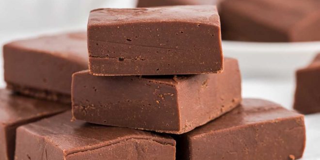 Dunkle, glänzende Quadrate von Schokoladen-Fudge auf einem rustikalen Holzbrett angerichtet.