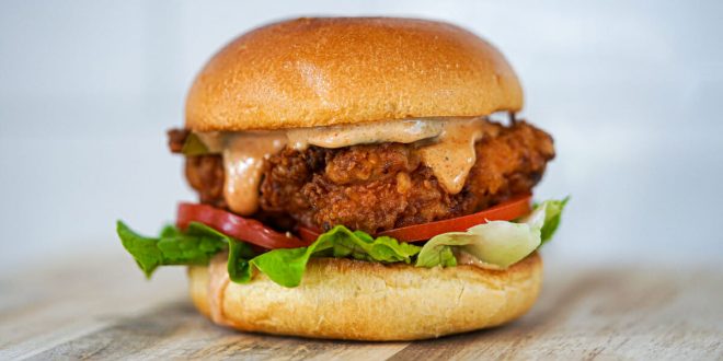 Ein aufgetürmtes Buttermilk Fried Chicken Sandwich in einem Brioche-Bun mit schmelzendem Käse und buntem Coleslaw.